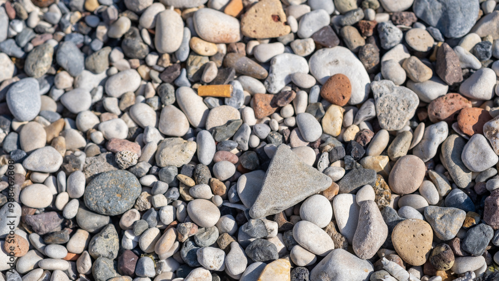 A diverse collection of small stones and pebbles lies on the beach, glistening in bright sunlight on a sunny afternoon A diverse collection of small stones and pebbles lies on the beach, glistening in bright sunlight on a sunny afternoon