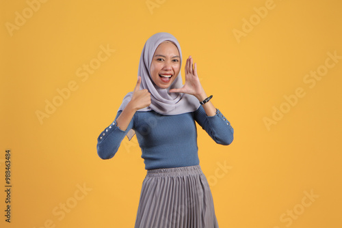 asian indonesian muslim woman shouting and giving thumb up finger gesture on isolated yellow bakcground photo