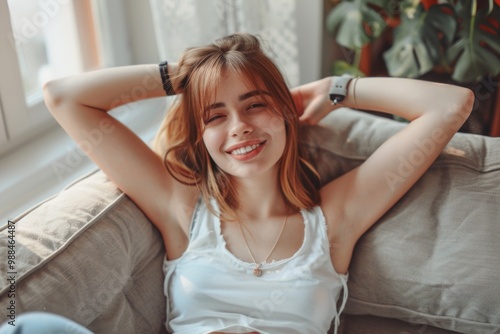 A woman sits comfortably on a couch with her hands behind her head, appearing relaxed and at ease