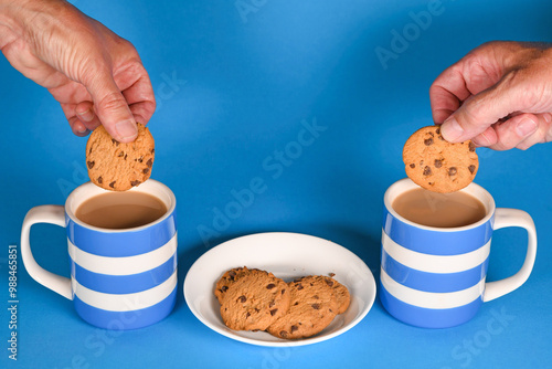 Foto Blue and white cups of tea with hands dunking a chocolate chip biscuit cookie
