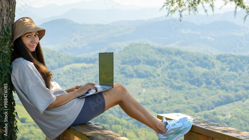 A young woman is working on a laptop in nature against the background of mountains photo