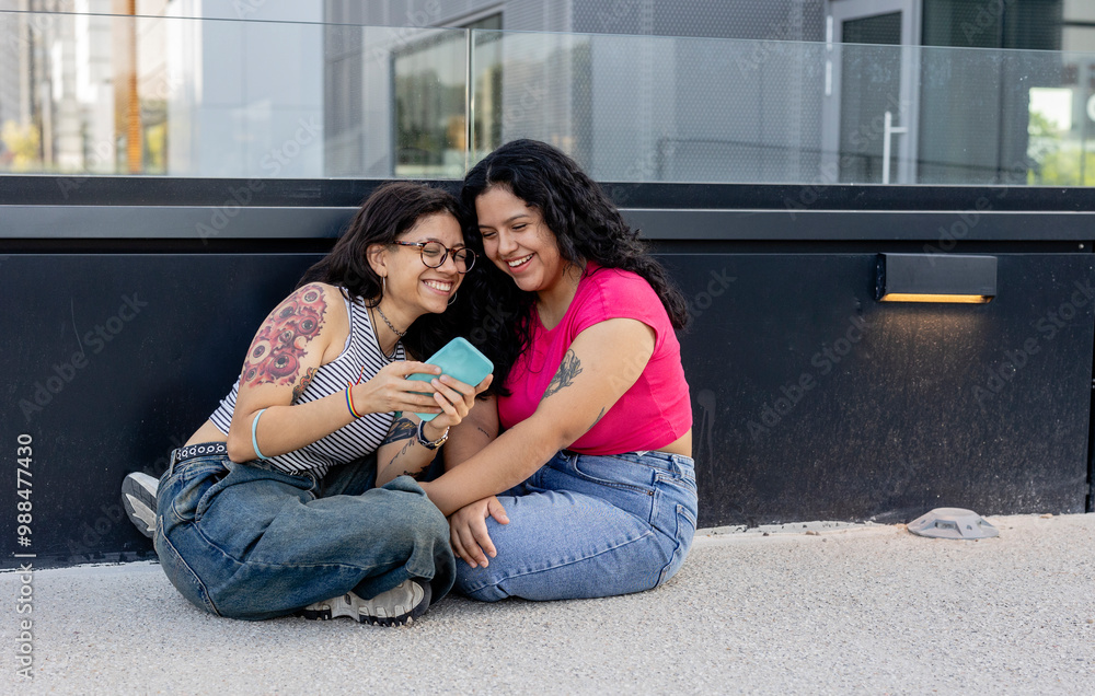 Happy lesbian couple using smart phone and sitting on ground Happy lesbian couple using smart phone and sitting on ground
