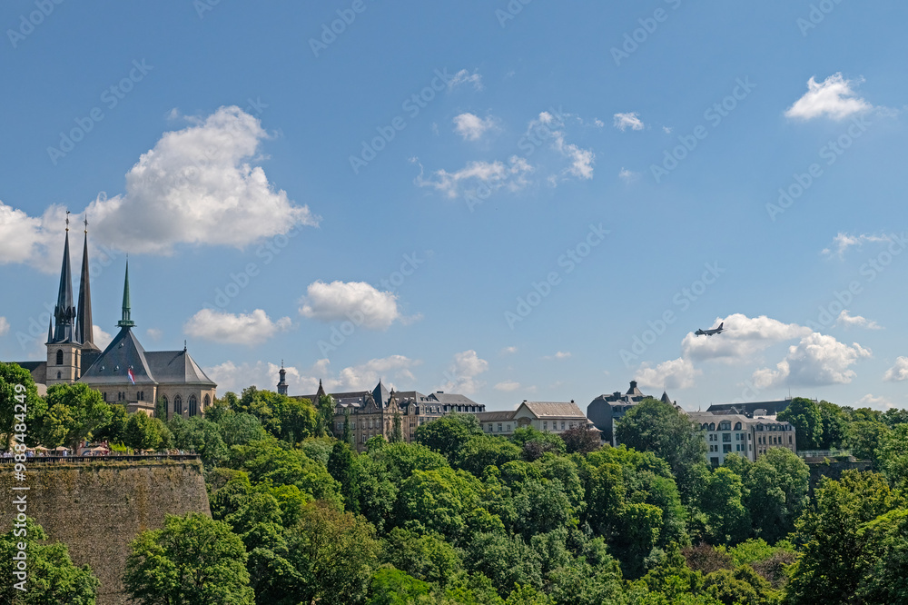 Fototapeta premium Cityscape in Luxembourg, passenger plane in blue and cloudy sky. Holiday and travel concept.