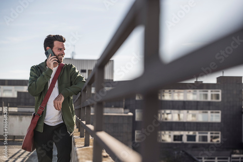 Smiling man talking on mobile phone near railing photo