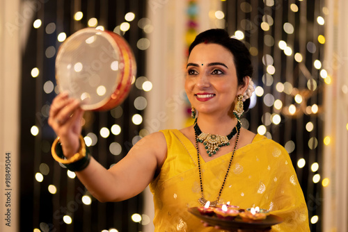 Beautiful Indian woman looking through sieve performing traditional Karwa Chauth ceremony photo