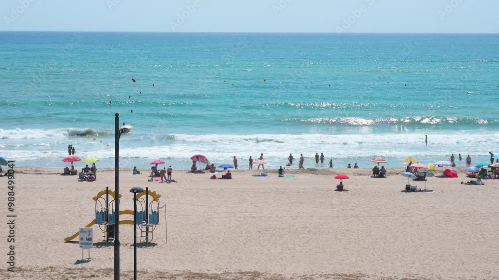Panoramic view of beachgoers and sunbathers at El Campello, Costa Blanca, Alicante, with swimmers frolicking near the Mediterranean Sea’s edge in Spain. Panoramic view of beachgoers and sunbathers at El Campello, Costa Blanca, Alicante, with swimmers frolicking near the Mediterranean Sea’s edge in Spain.