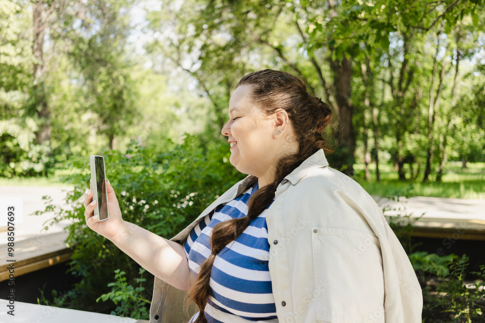 Smiling woman video calling using smart phone at public park Smiling woman video calling using smart phone at public park