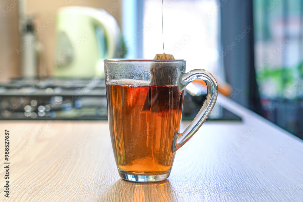 Freshly brewed tea is gently steaming in a clear glass cup on the kitchen counter Freshly brewed tea is gently steaming in a clear glass cup on the kitchen counter
