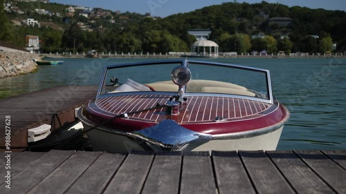 View of a speedboat moored to the pier and bobbing on the waves of the lake in the evening, the boat is tied with a rope to a wooden pier. A small luxury pleasure boat moored to a pier on a small lake photo