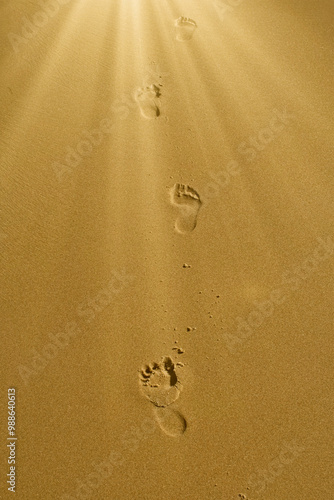 Footprints in the sand walking forward into a sunbeam. photo