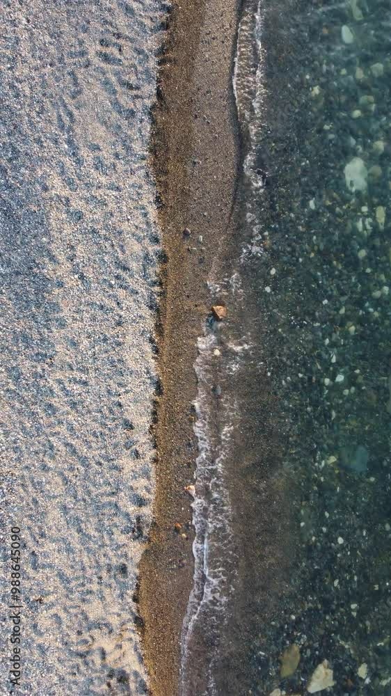 Aerial vertical view of beach with wave caressing shore. Sun glare, small waves on the water surface. Sunset. Evening. Nobody. No people. Summer travel and vacation. Aerial vertical view of beach with wave caressing shore. Sun glare, small waves on the water surface. Sunset. Evening. Nobody. No people. Summer travel and vacation.