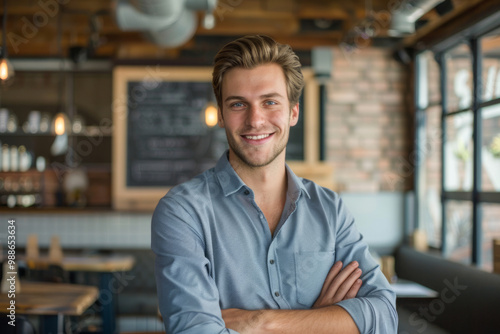 Young man smiling confidently in front of a company logo within a modern café setting during the daytime