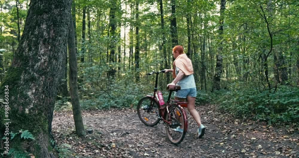 A cyclist is peacefully rolling along a serene forest path, surrounded by greenery and bright fallen leaves. A cyclist is peacefully rolling along a serene forest path, surrounded by greenery and bright fallen leaves.