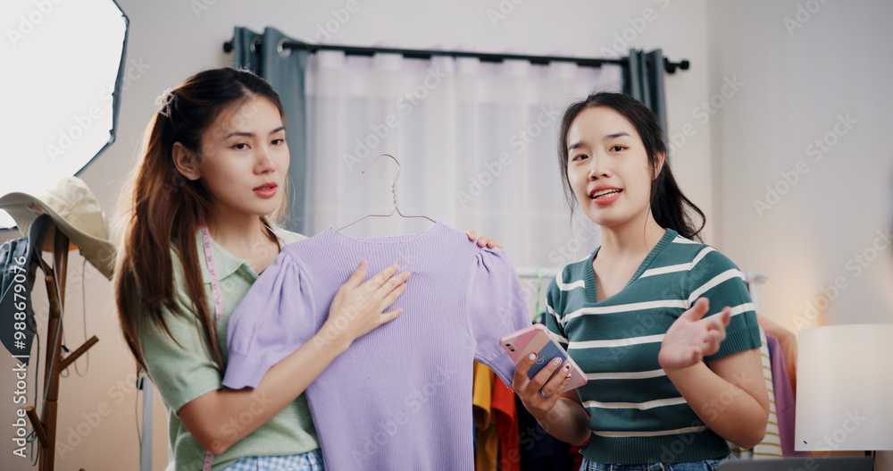 Obraz premium Portrait of Two cheerful woman influencers are live streaming sell clothes on social media or blogging in home studio. Remote buying, Online shopping, Sell ​​products online