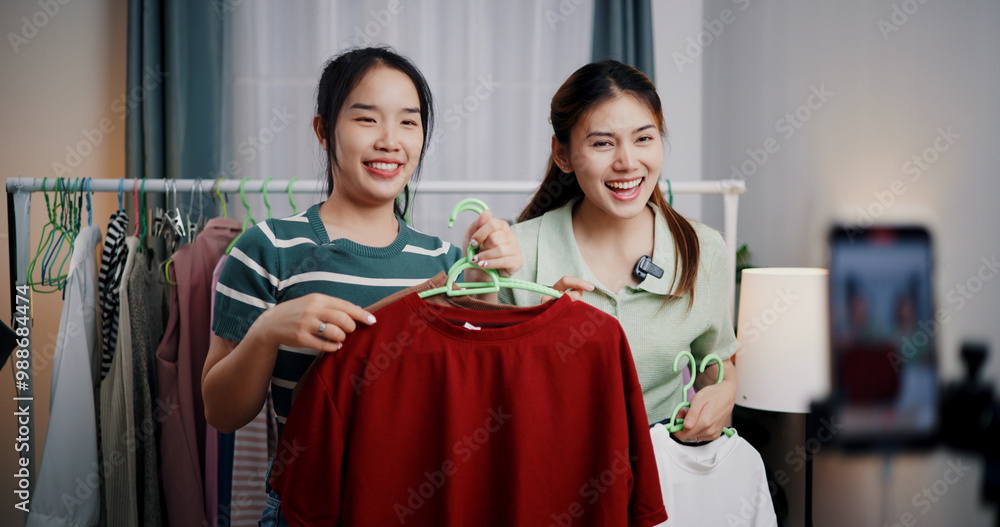 Obraz premium Portrait of Two cheerful woman influencers are live streaming sell clothes on social media or blogging in home studio. Remote buying, Online shopping, Sell ​​products online