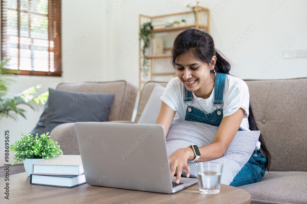 Young Woman Working on Laptop at Home, Smiling and Relaxed in a Cozy Living Room Setting with Natural Light Young Woman Working on Laptop at Home, Smiling and Relaxed in a Cozy Living Room Setting with Natural Light