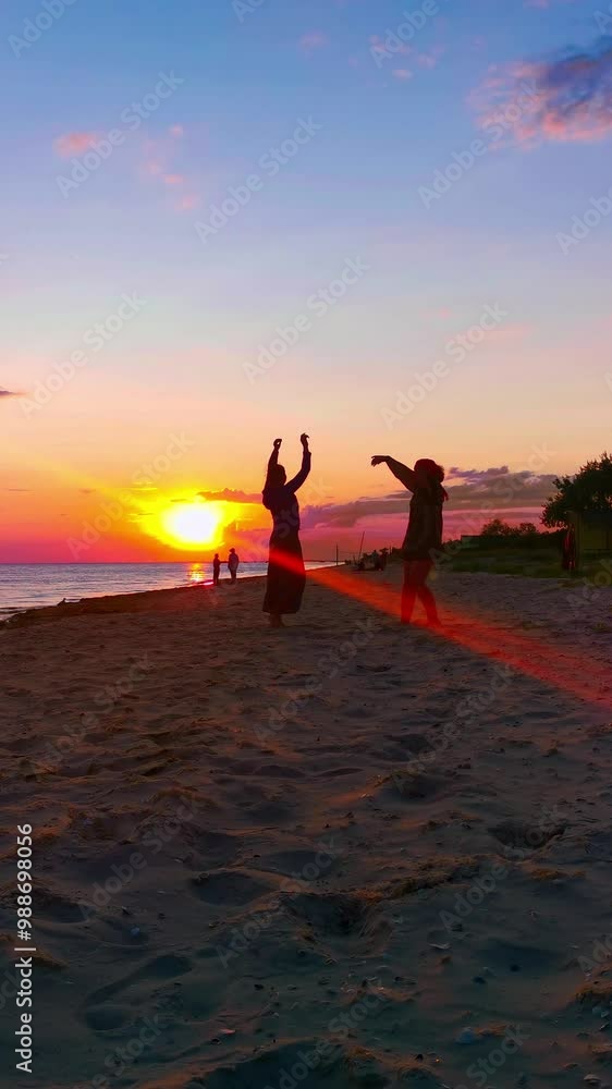 Two women dancing on the beach in front of the sunset. Vertical video Two women dancing on the beach in front of the sunset. Vertical video