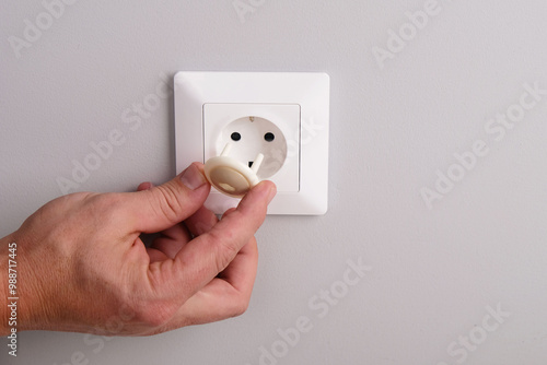 A hand installs a protective plug into an electrical outlet to protect children from electric shock.