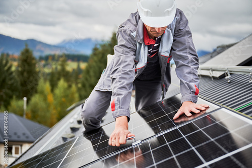 Man engineer mounting photovoltaic solar panels on roof of house. Technician in helmet installing solar module system with help of hex key. Concept of alternative, renewable energy. photo