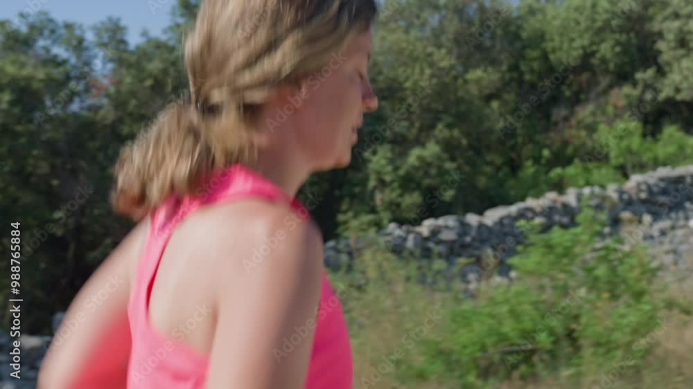 Woman jogging on rocky trail surrounded by lush greenery and trees under clear blue sky. Female sportsman running cross country on hot summer day. Endurance training Woman jogging on rocky trail surrounded by lush greenery and trees under clear blue sky. Female sportsman running cross country on hot summer day. Endurance training
