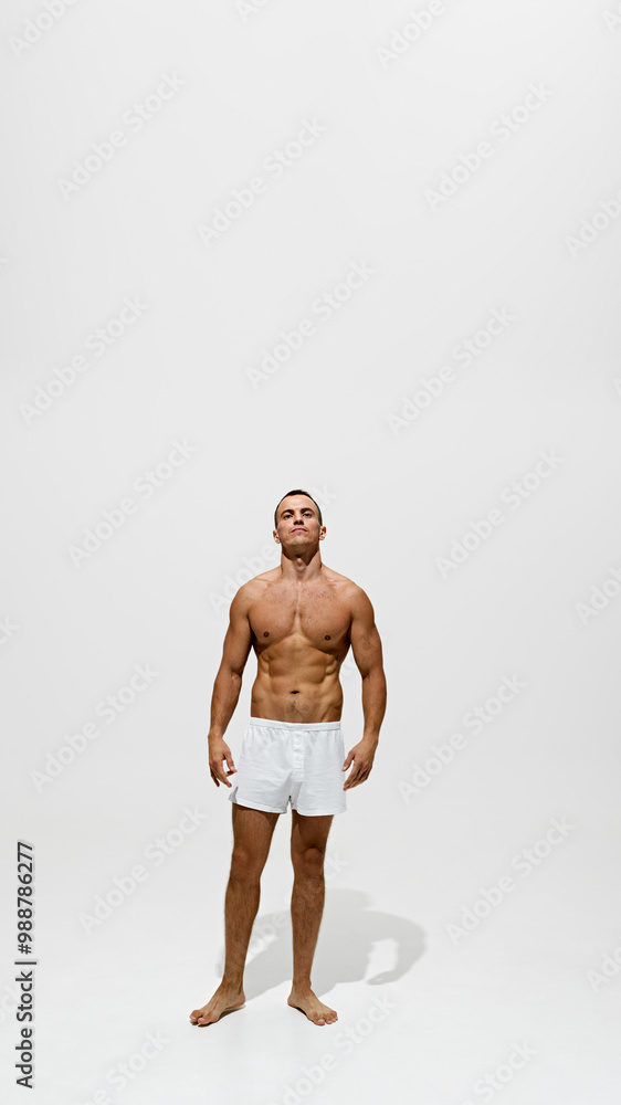 Fototapeta premium Full-length portrait of handsome man posing shirtless in underwear, showing his perfect, muscular, strong body isolated on white background. Concept of male beauty, body and skin care, health, sport