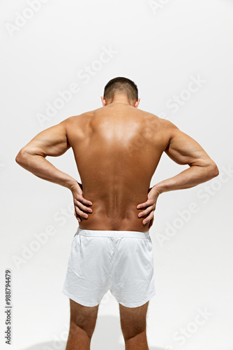 Back pain reduction. Rear view of shirtless man posing in underwear isolated on white studio background. Muscular, relief body. Concept of male beauty, body and skin care, health, sport