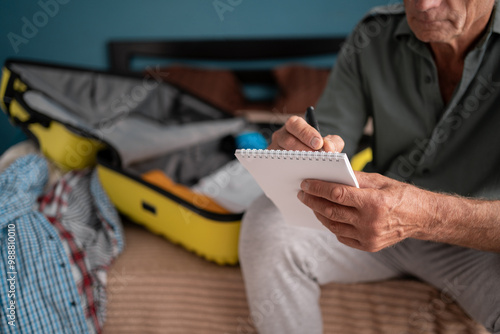 Vacation, holiday and travel concept. Man writing check list note after packing luggage or baggage for journey trip sitting at home photo