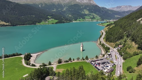 The famous bell tower in Italy with a mountain backdrop and surrounding area, road, and vehicles, Curon, Italy photo