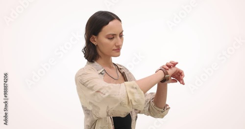 Woman checks wristwatch and continues to wait for unpunctual boyfriend on white background. Female feels mix of concern and frustration photo