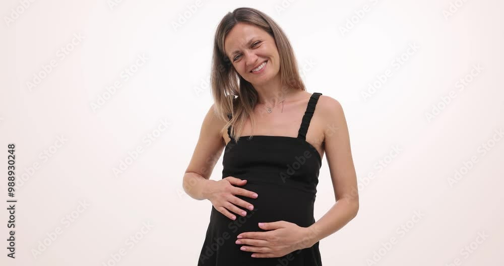Pregnant woman with radiant smile places hands on belly on white background. Pregnant female feels subtle movements of expected baby slow motion Pregnant woman with radiant smile places hands on belly on white background. Pregnant female feels subtle movements of expected baby slow motion