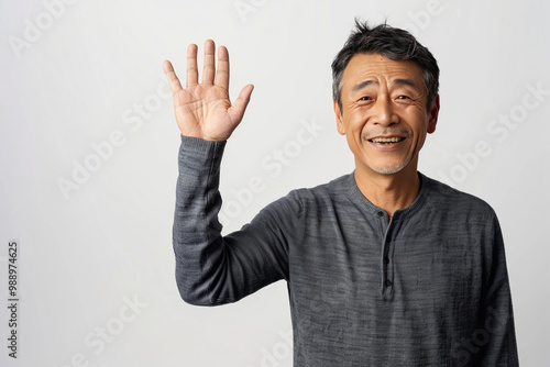 A Chinese man look in the camera, friendly wave and a friendly smile in front of neutral white backdrop.