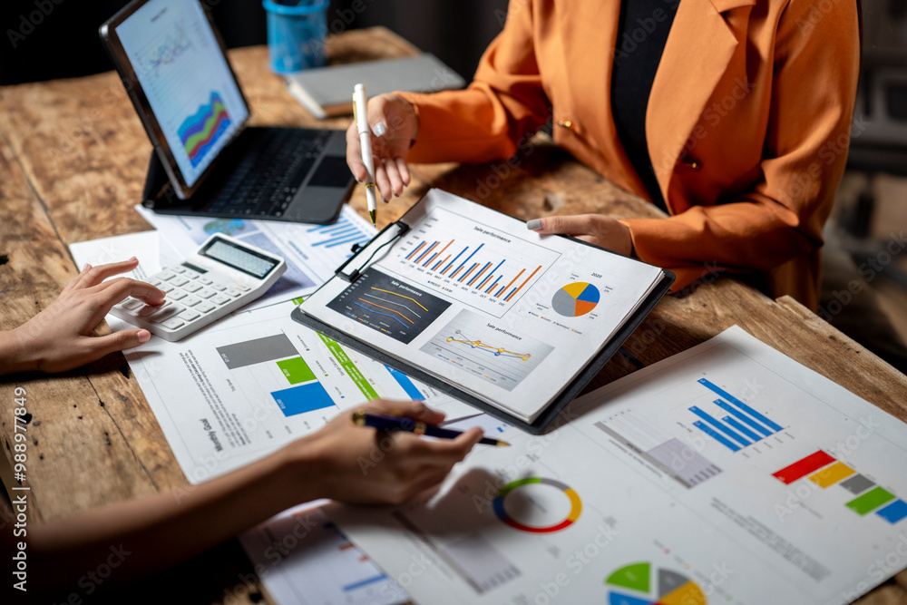 Businesswomen analyzing financial charts and using calculator in a meeting Businesswomen analyzing financial charts and using calculator in a meeting
