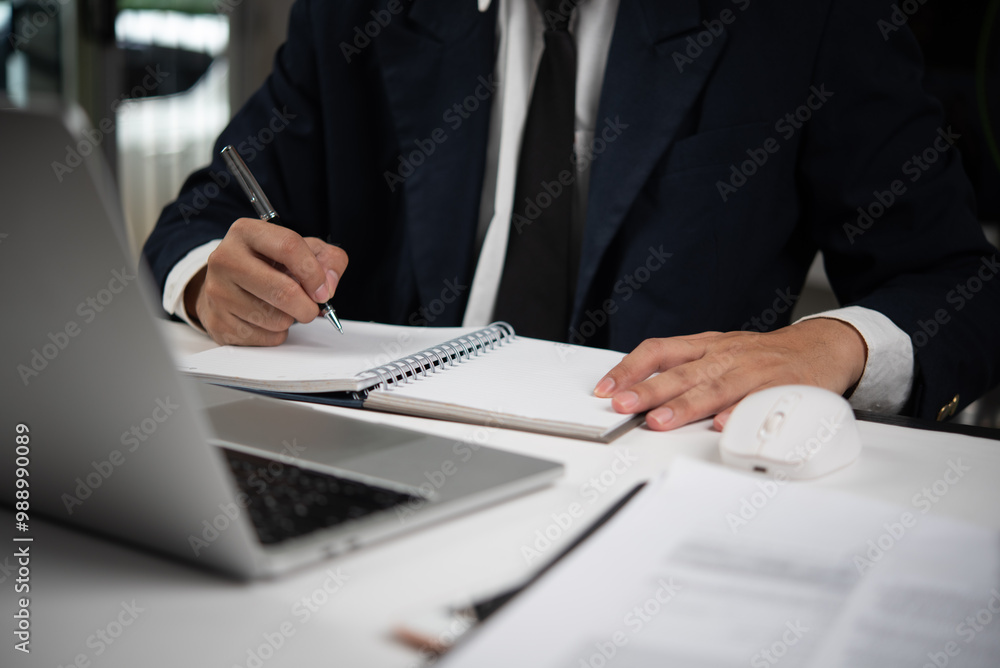 Businessman writing in notebook with laptop on desk Businessman writing in notebook with laptop on desk