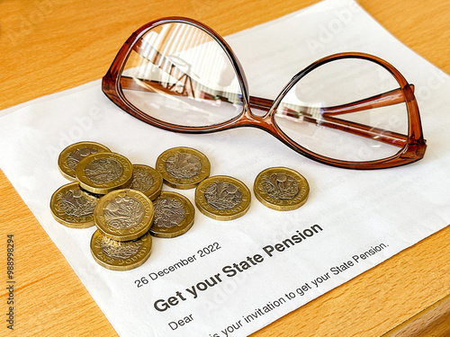 Offical letter telling a person of state retirement age in the UK they can get their pension, with one pound coins and a pair of reading glasses. photo