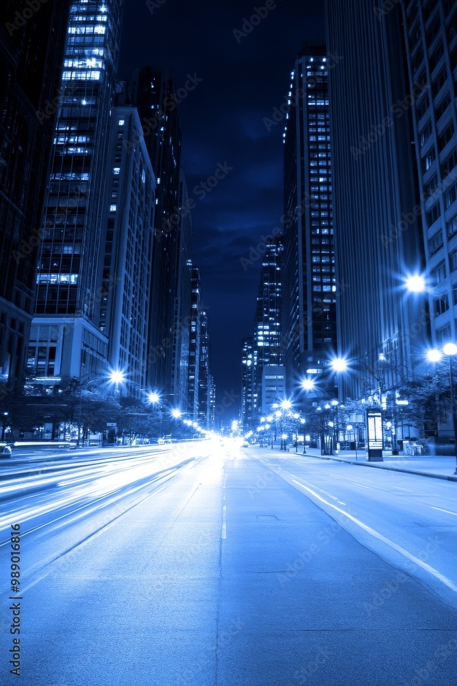Obraz premium A stunning night view of a bustling city street, illuminated by blue tones and glowing lights.