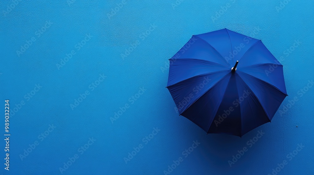 A single, bold blue umbrella placed against a matching blue background, offering a minimalist and modern composition. A single, bold blue umbrella placed against a matching blue background, offering a minimalist and modern composition.