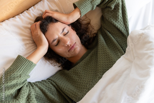 Lying in bed, woman holding head and experiencing headache or stress