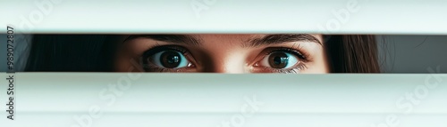 A close-up of a pair of curious eyes peering through blinds, creating a sense of mystery and intrigue.