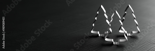 Three Christmas Tree cookie cutters standing on a wooden black table. Web banner size. Copy space photo