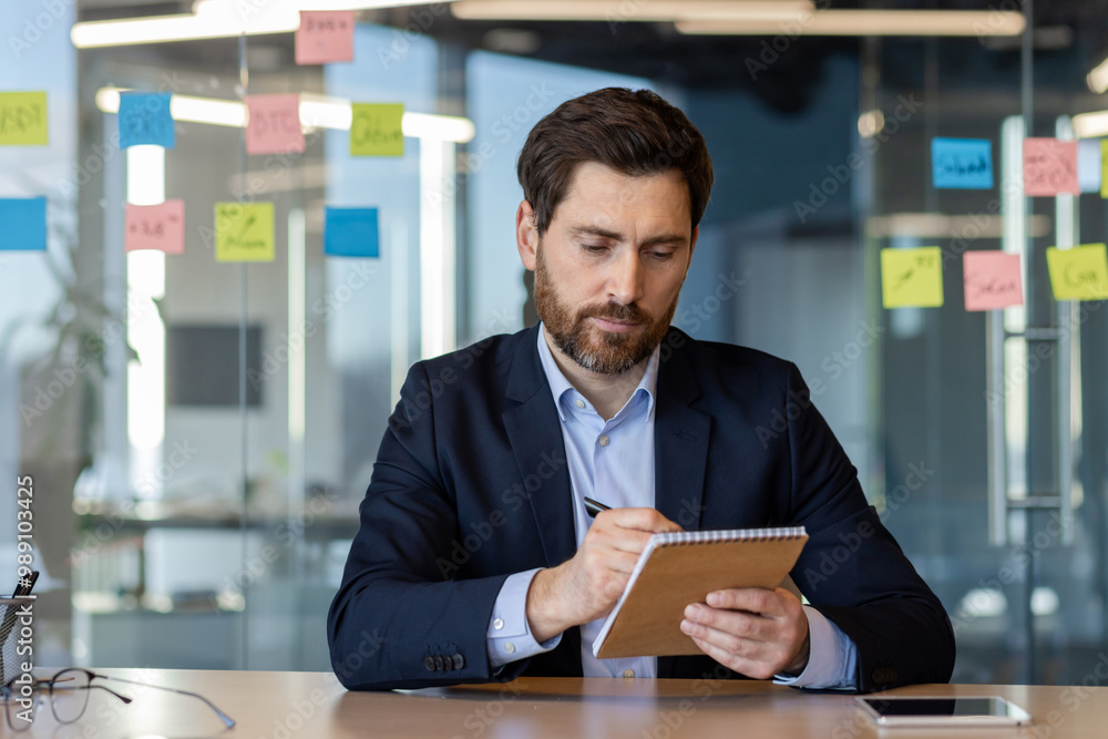 Focused business professional writing in notebook during meeting. Modern office environment with colorful sticky notes in background. Concept planning, organization, concentration, and productivity. Focused business professional writing in notebook during meeting. Modern office environment with colorful sticky notes in background. Concept planning, organization, concentration, and productivity.