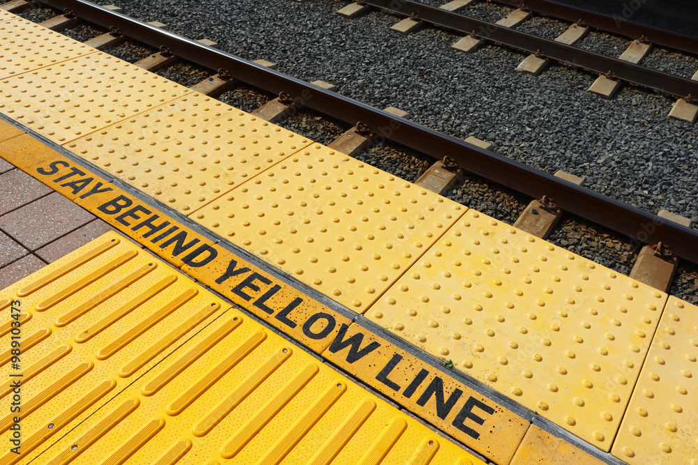Stay Behind Yellow Line Warning Sign on platform at Train Station