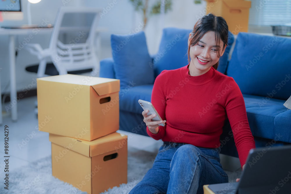Young woman is using her laptop and smartphone while sitting on the floor of her new apartment, surrounded by cardboard boxes Young woman is using her laptop and smartphone while sitting on the floor of her new apartment, surrounded by cardboard boxes