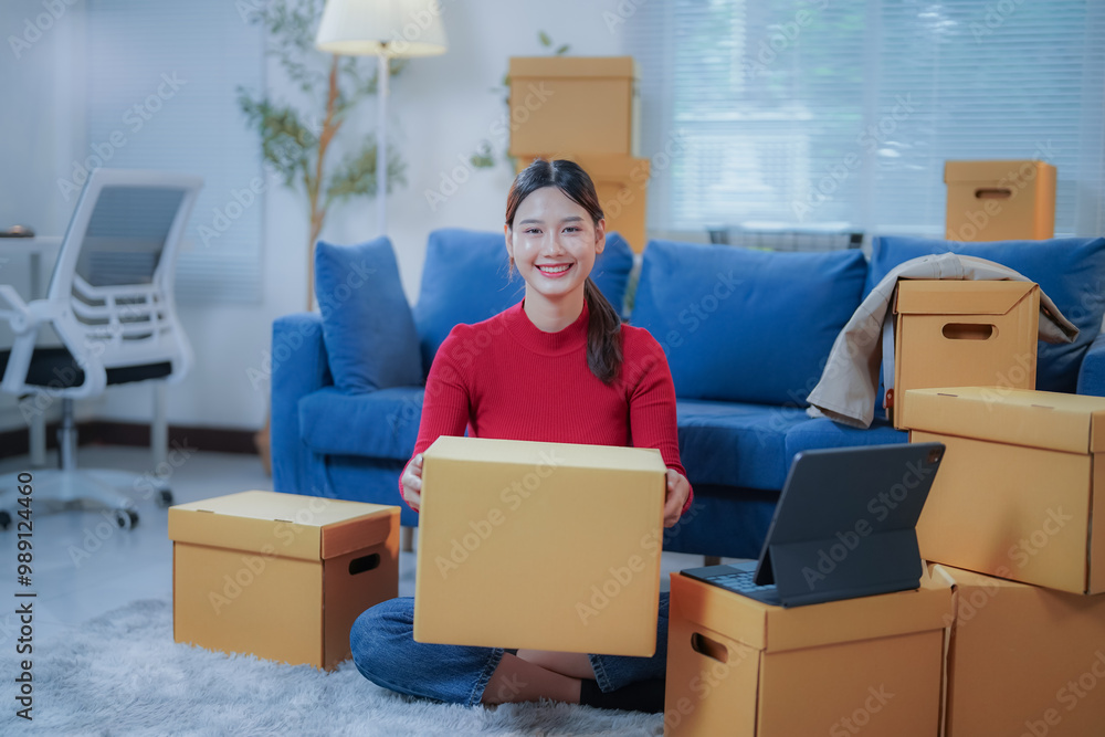 Young asian woman entrepreneur, startup, sme owner, working in her living room at home, packing cardboard boxes, preparing online orders for delivery to customers Young asian woman entrepreneur, startup, sme owner, working in her living room at home, packing cardboard boxes, preparing online orders for delivery to customers