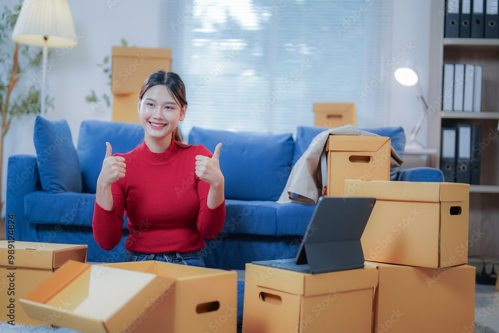 Young asian woman is showing thumbs up while sitting on the floor of her living room, surrounded by cardboard boxes and using a digital tablet Young asian woman is showing thumbs up while sitting on the floor of her living room, surrounded by cardboard boxes and using a digital tablet