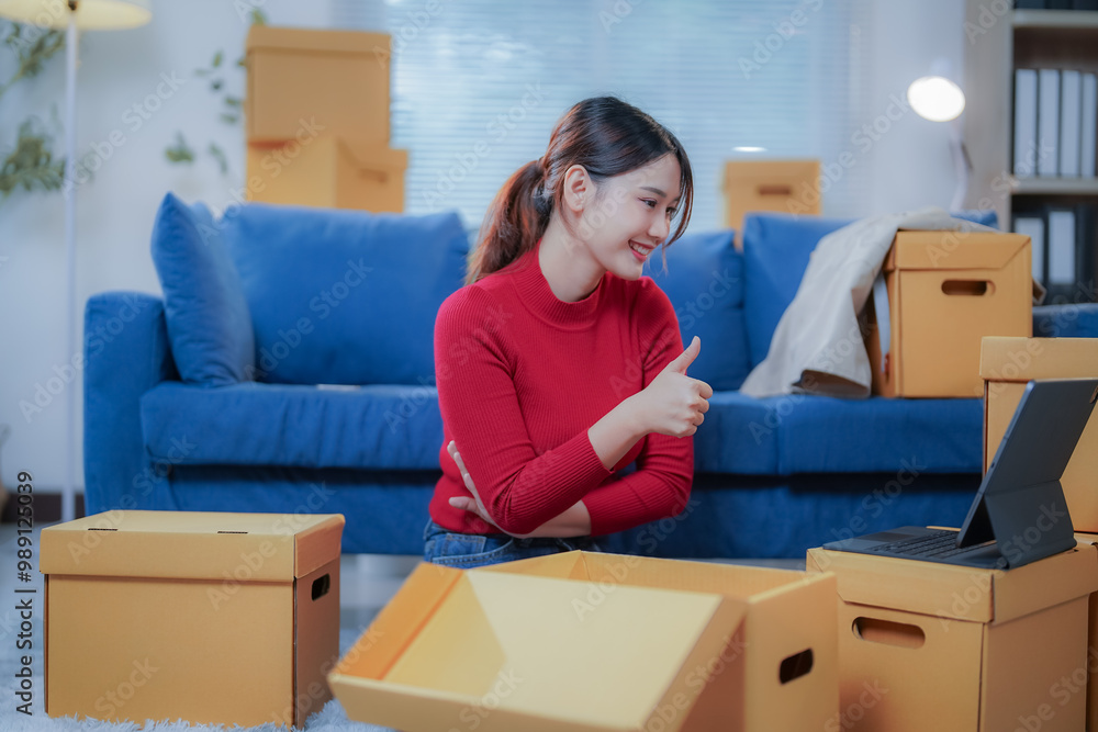 Young asian woman is working in a warehouse and showing thumbs up during a video call on a tablet, surrounded by cardboard boxes Young asian woman is working in a warehouse and showing thumbs up during a video call on a tablet, surrounded by cardboard boxes