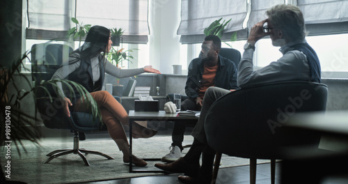 Asian woman sits on chair, talks to psychologist about relationship with her boyfriend during counseling session. Mature psychotherapist listens to multiethnic young family, provides couples therapy.