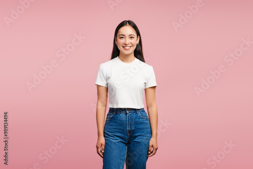 Smiling, attractive Asian woman smiling wearing white t-shirt and jeans on pink background