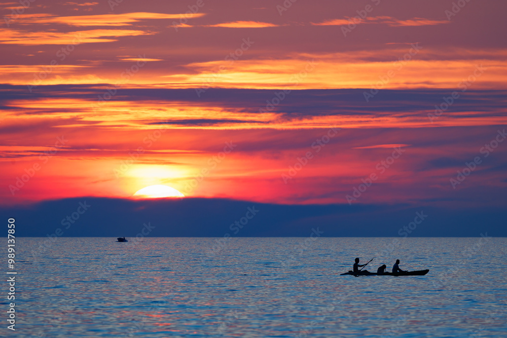 Fototapeta premium A sunset over the ocean with a canoe in the water, Thailand