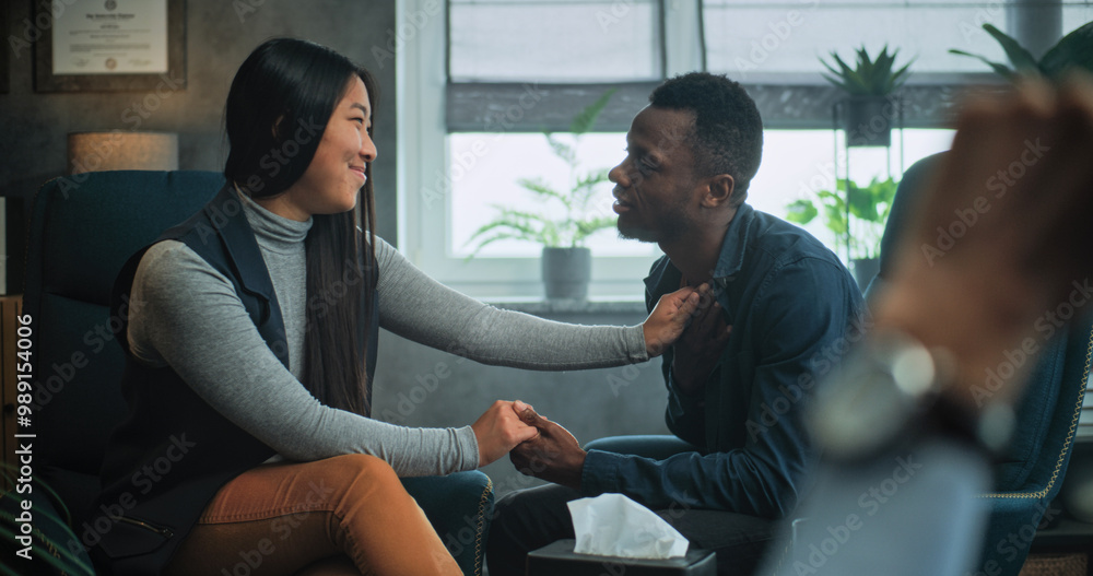 Happy multiethnic couple sit on chairs holding hands and hugging, talk, find compromise after fight on couples therapy. Close up of therapist looking at tender young family on counseling session. Happy multiethnic couple sit on chairs holding hands and hugging, talk, find compromise after fight on couples therapy. Close up of therapist looking at tender young family on counseling session.