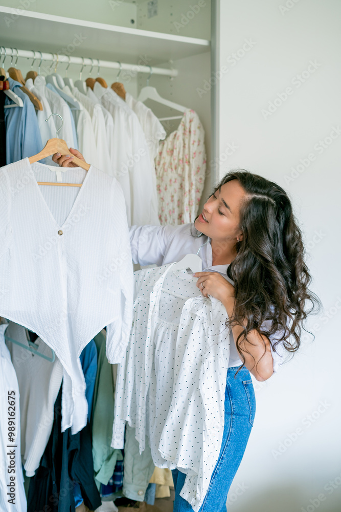 Young dark-haired curly beautiful woman is sorting things in large spacious closet. Home organization. Washing things. Analysis of clothes by season. Young dark-haired curly beautiful woman is sorting things in large spacious closet. Home organization. Washing things. Analysis of clothes by season.